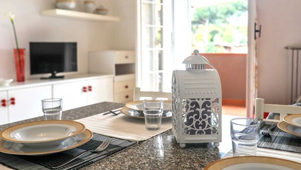 A well-lit kitchen with a dining table set for two, a television, and a decorative lantern. - [ZONA POETI] ★★★★★ Relax in Piscina - Free Parking (Loano)