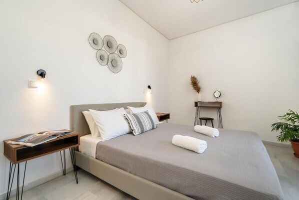 A modern bedroom with a large bed, bedside tables, a wall-mounted light fixture, and a decorative wall piece. - Flerianos Studios (Naxos)