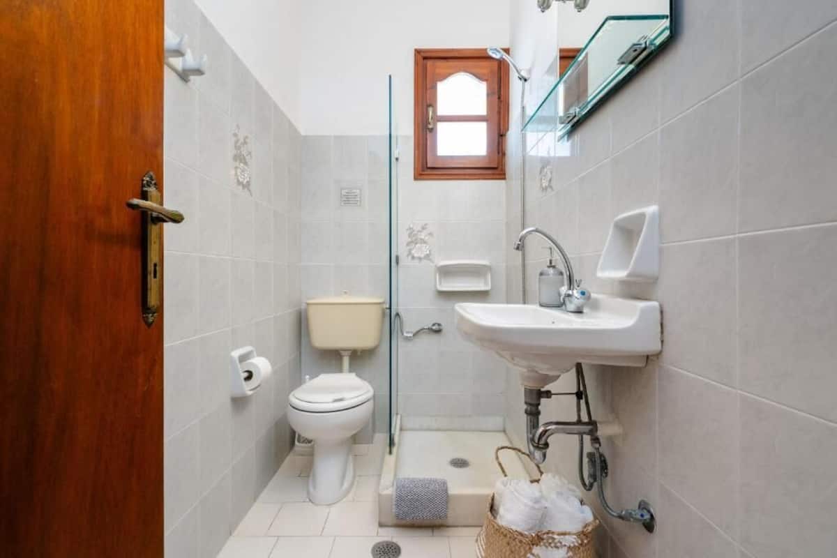 A bathroom with a toilet, sink, shower, and a wooden door.