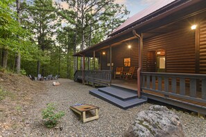 Relax on the covered porch amidst a serene forest setting, surrounded by trees and a natural landscape.
