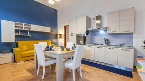 A modern kitchen with white cabinets, a gas stove, and a built-in oven. There is a dining table with white chairs and a yellow sofa in the living area. - Rhome 14 Smart workers cozy apt (Rho)