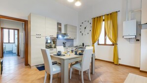A modern kitchen with white cabinets, a stainless steel range hood, and a built-in oven. There is a dining table with chairs and a yellow curtain covering the window. - Rhome 14 Smart workers cozy apt (Rho)