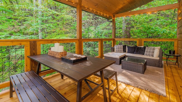 An outdoor deck with a wooden table, benches, and a sofa with patterned cushions. - 🌅 Bear Valley Splash 🍃 Indoor Pool, Creekside Yard, Hot Tub & Games (Sevierville)