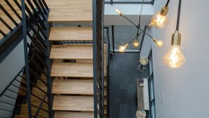 Una escalera de madera con barandas negras que lleva a una habitación con pared negra y lámparas colgantes.