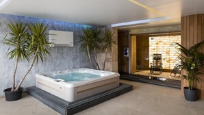 Un área de spa moderna con un jacuzzi, plantas en macetas y una zona de estar con vistas al exterior.
