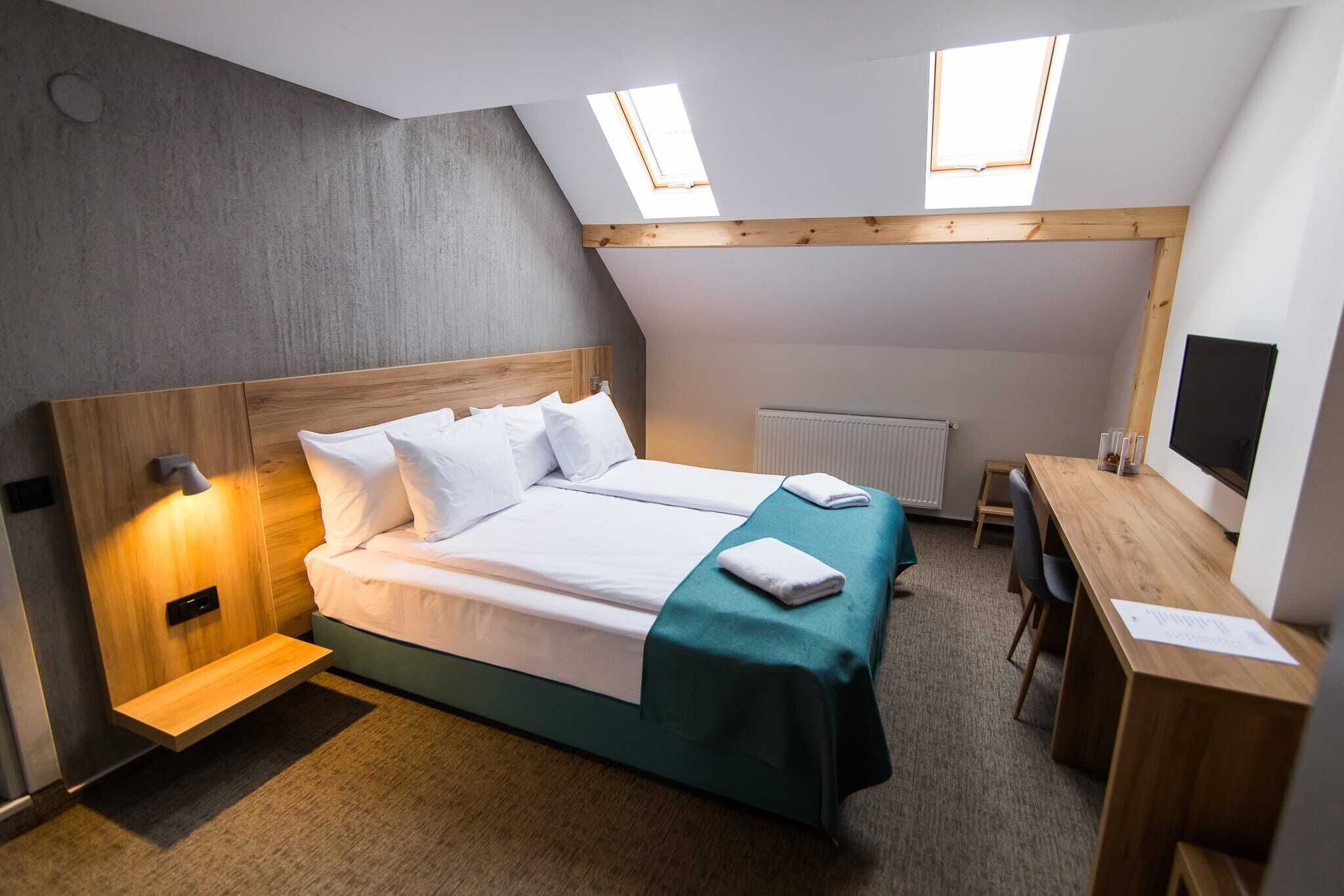 A bedroom with a bed, a desk, a chair, a radiator, and a TV.