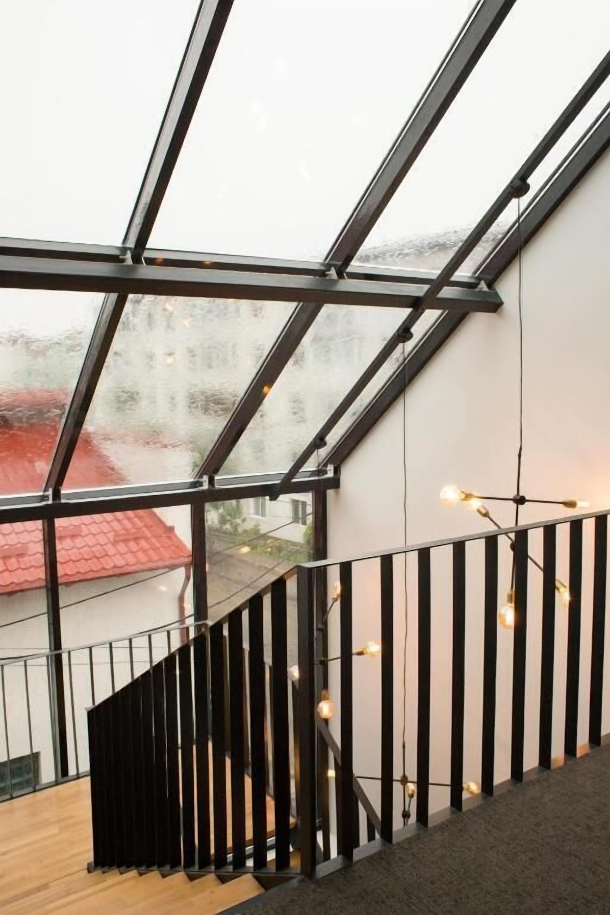 A modern interior with a glass ceiling, a wooden staircase, and a view of a red-roofed building outside.