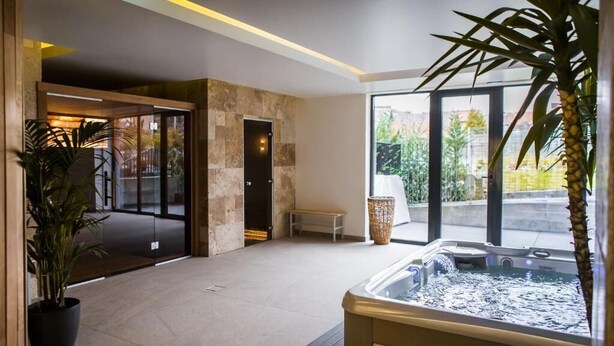Un moderno espacio de spa con un jacuzzi, una banca y un amplio ventanal con vistas al exterior.