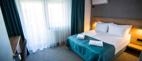 Habitación de hotel con cama, escritorio y ventana con cortinas.