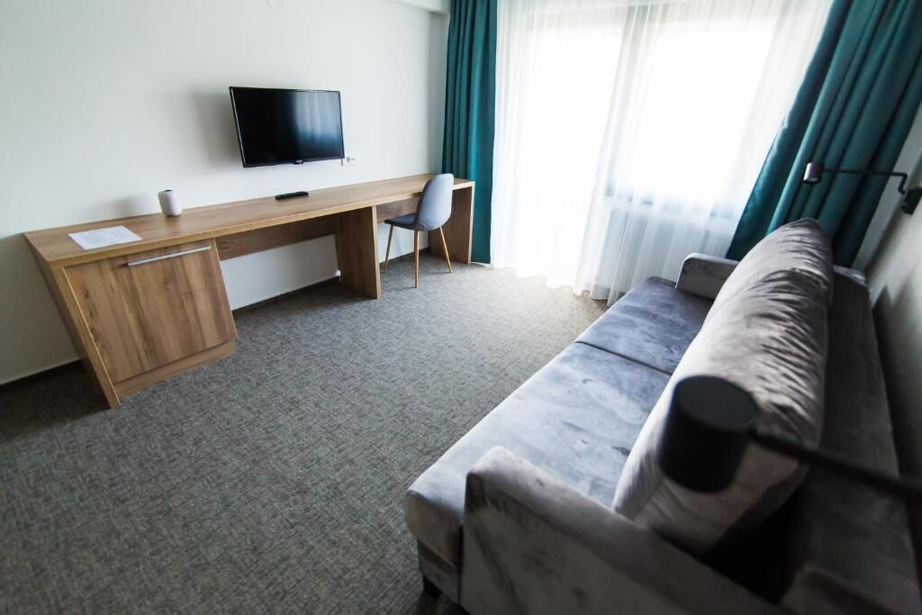 Una habitación de hotel con un escritorio de madera, un televisor, un sofá gris y una ventana con cortinas.