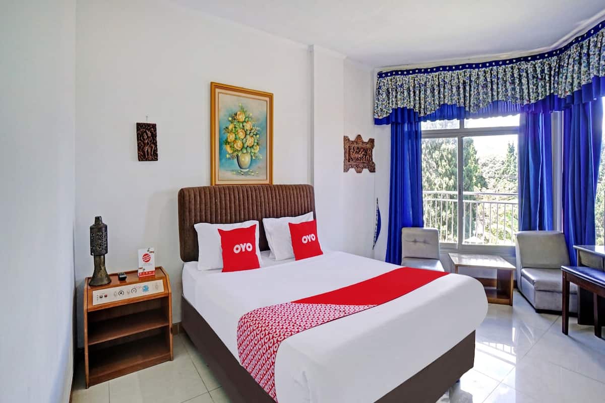 Een hotelkamer met een groot bed, een nachtkastje met een lamp, een schilderij aan de muur en uitzicht op het omliggende landschap door het raam.