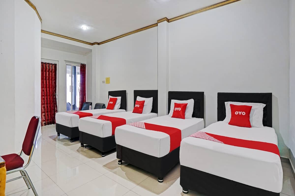 Een hotelkamer met vier bedden op een rij, elk met een rode en witte dekbedovertrek en kussens.
