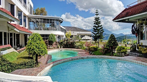 A resort with a swimming pool, a mountain view, and a building with a curved glass facade.