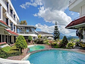 Un complexe hôtelier doté d’une piscine, offrant une vue sur la montagne, et dont le bâtiment se distingue par sa façade en verre incurvé.