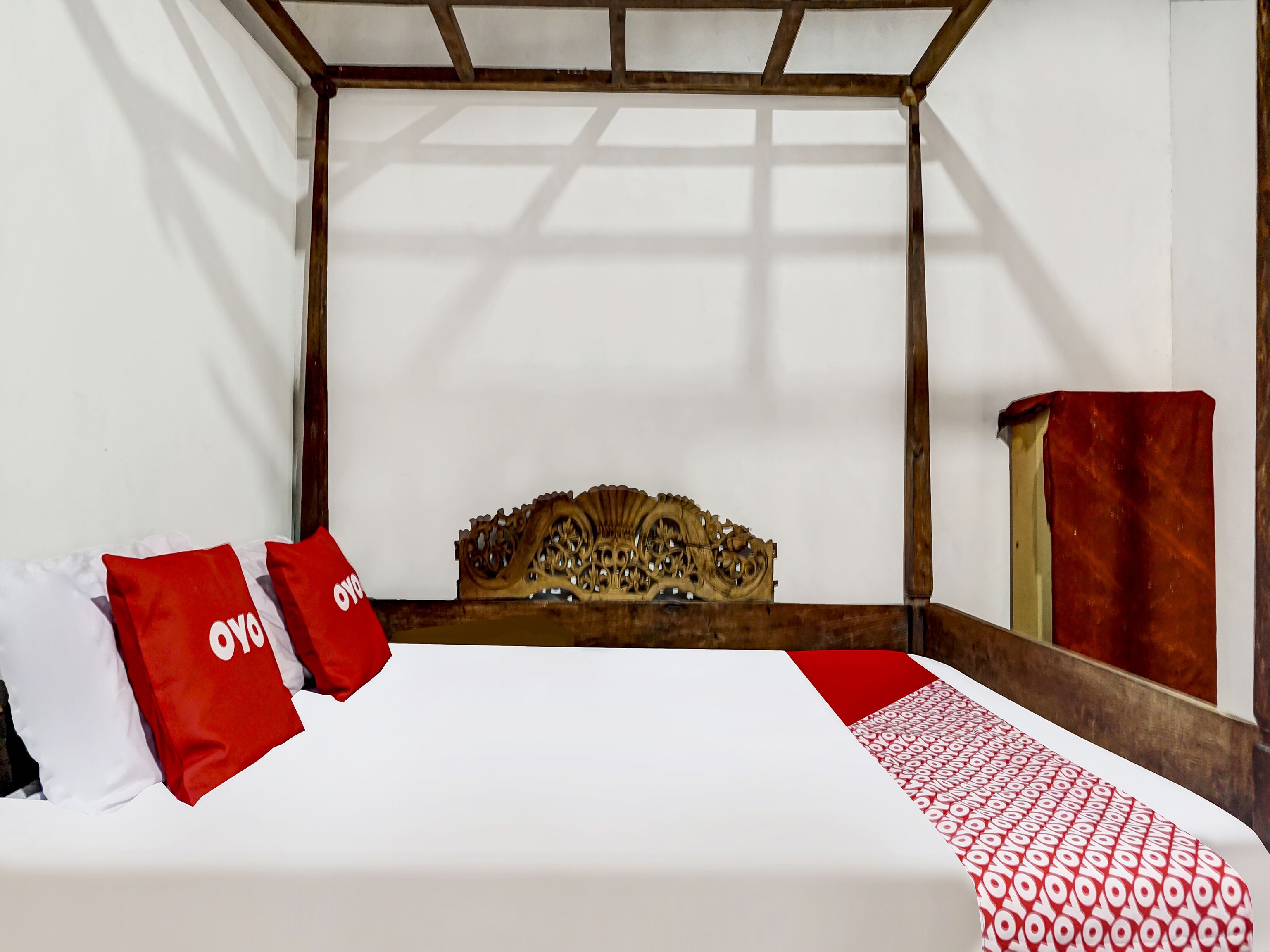 A bed with a wooden headboard, white bedding, and red pillows with "OVYO" text.