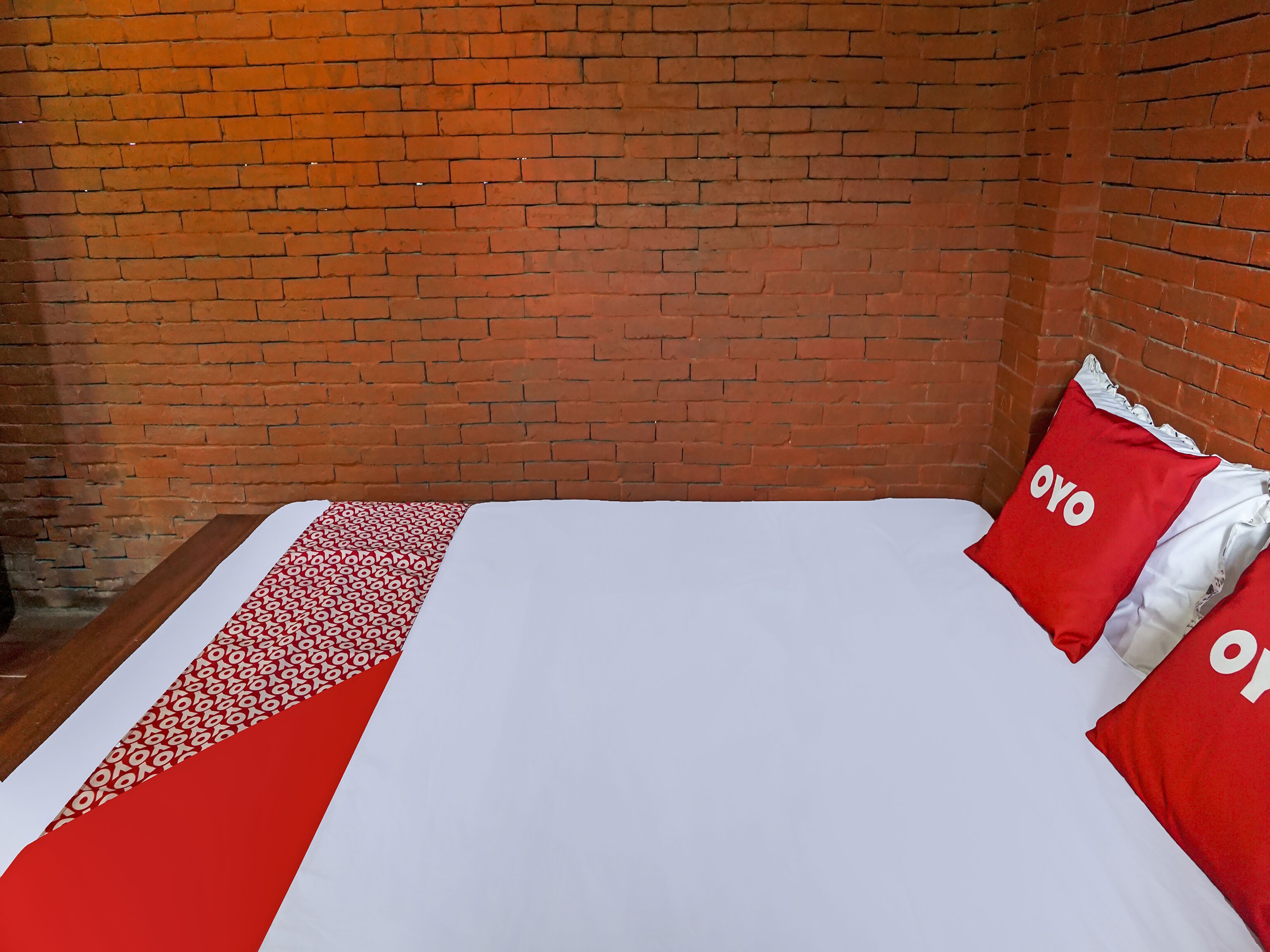 A hotel room with a brick wall, a bed with a white and red bedspread, and two pillows with the word "OYO" on them.