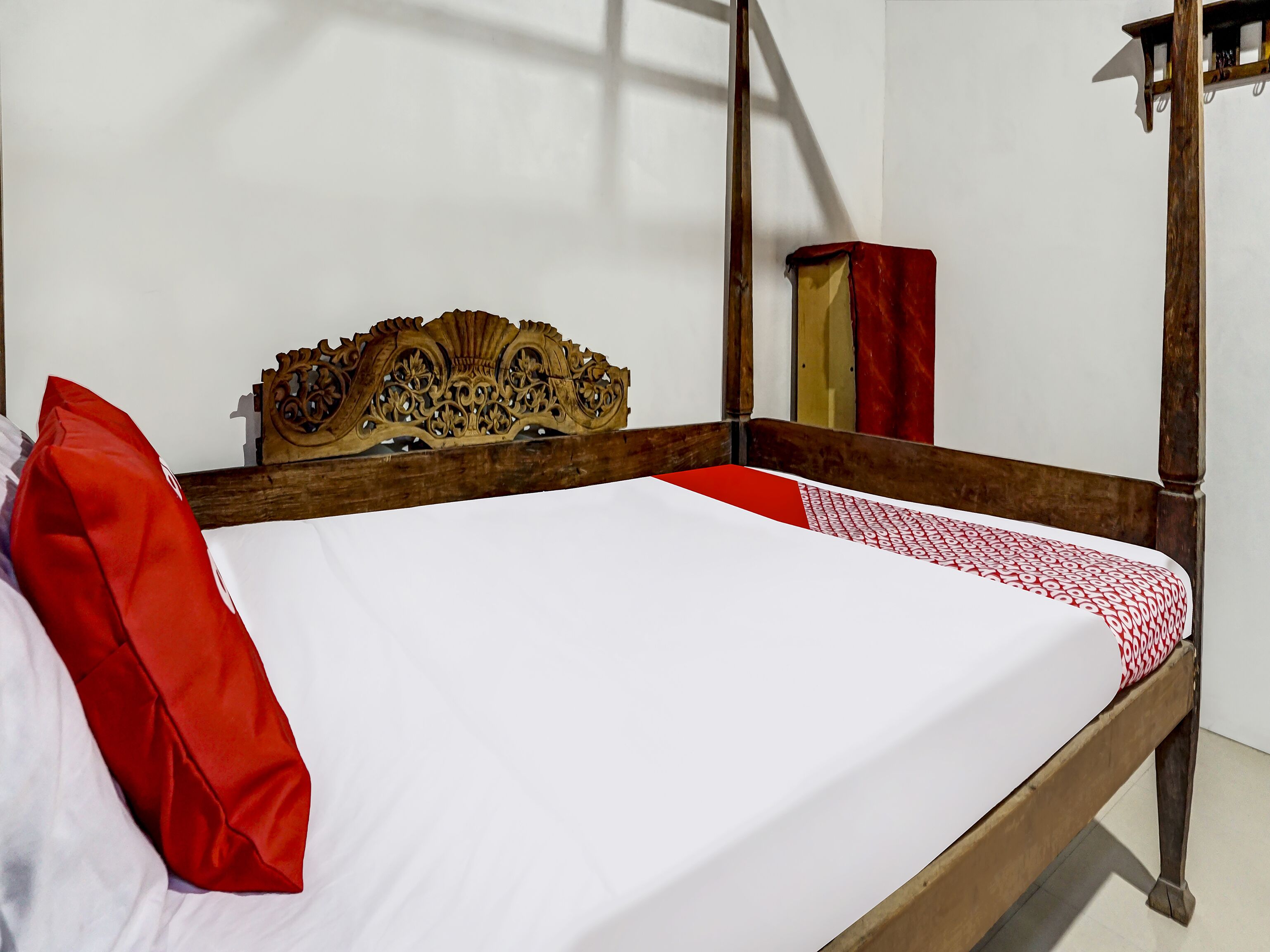A bed with a wooden headboard, a red pillow, and a patterned bedspread.