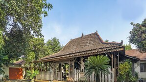 A traditional wooden structure with a tiled roof, surrounded by greenery and a paved area. - Hotel O Desa Wisata Kampung Majapahit (Bejijong)