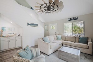 Un salon moderne avec un canapé d’angle, un fauteuil à rayures, une table basse en bois et un ventilateur de plafond.