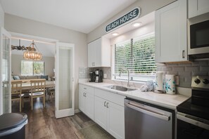 Een moderne keuken met witte kasten, een koffiezetapparaat en een raam met jaloezieën.