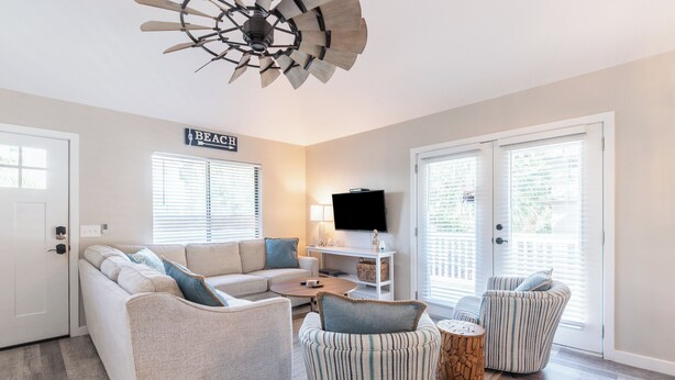 A modern living room with a beige sofa, striped armchairs, a coffee table, and a ceiling fan.