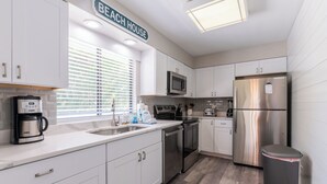 A modern kitchen with white cabinets, stainless steel appliances, a coffee maker, and a trash can.