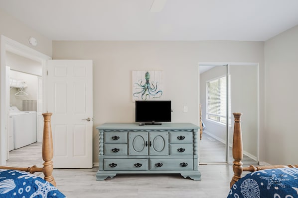 A bedroom with a dresser, a television, and a painting on the wall.