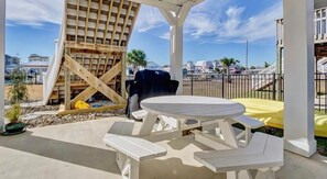 Un espace extérieur aménagé en terrasse, doté d’une pergola en bois, d’un barbecue et d’une table ronde avec des bancs.