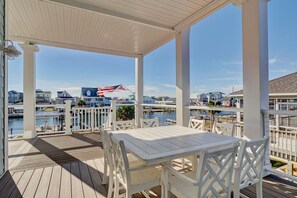 Une terrasse extérieure couverte, dotée d’une table et de chaises, qui offre une vue sur une marina avec des bateaux et des bâtiments situés au bord de l’eau.