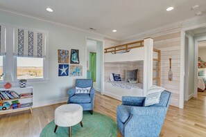Une chambre d’enfant avec un lit superposé, un fauteuil de lecture, un petit pouf et une bibliothèque remplie de jouets et de livres.