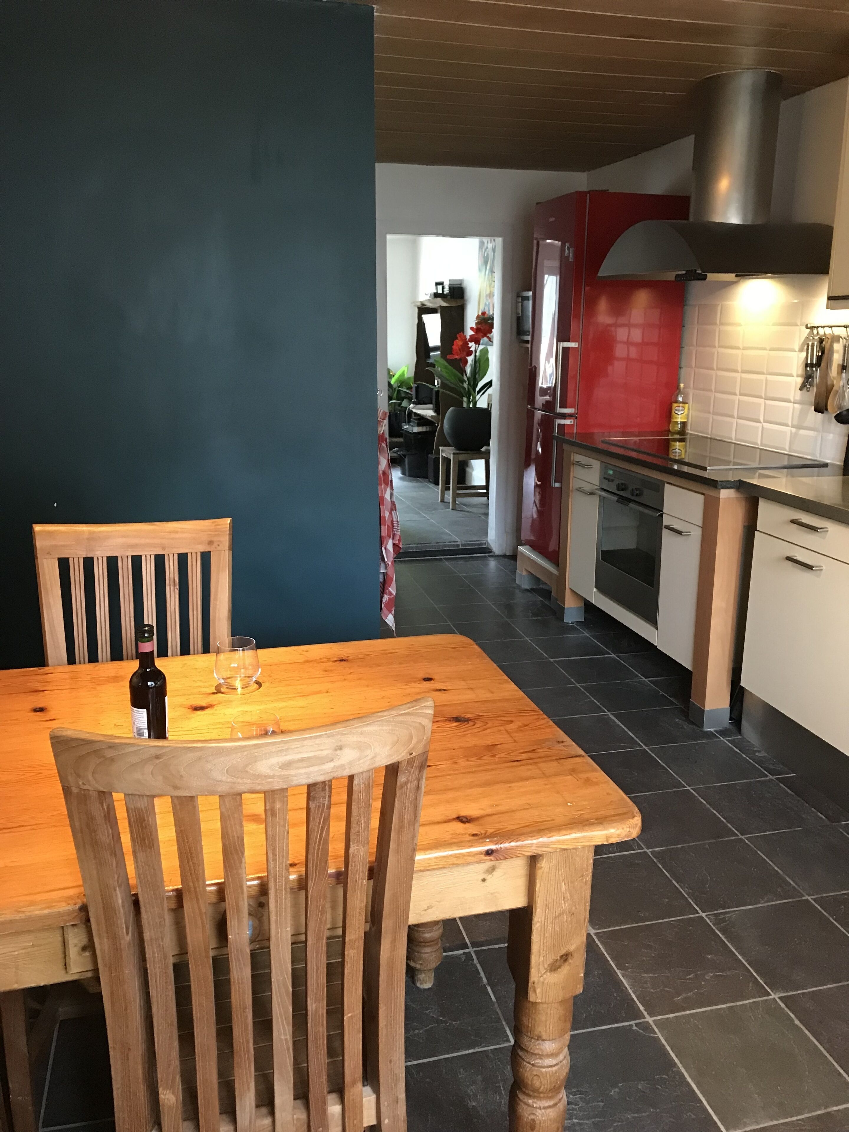A dining area with a wooden table and chairs, a bottle of wine, and a glass on the table.