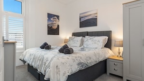 A bedroom with a bed, nightstands, a wardrobe, and two wall-mounted pictures. - Caldey Bay Apartment - Lovely Sea Views (Tenby)