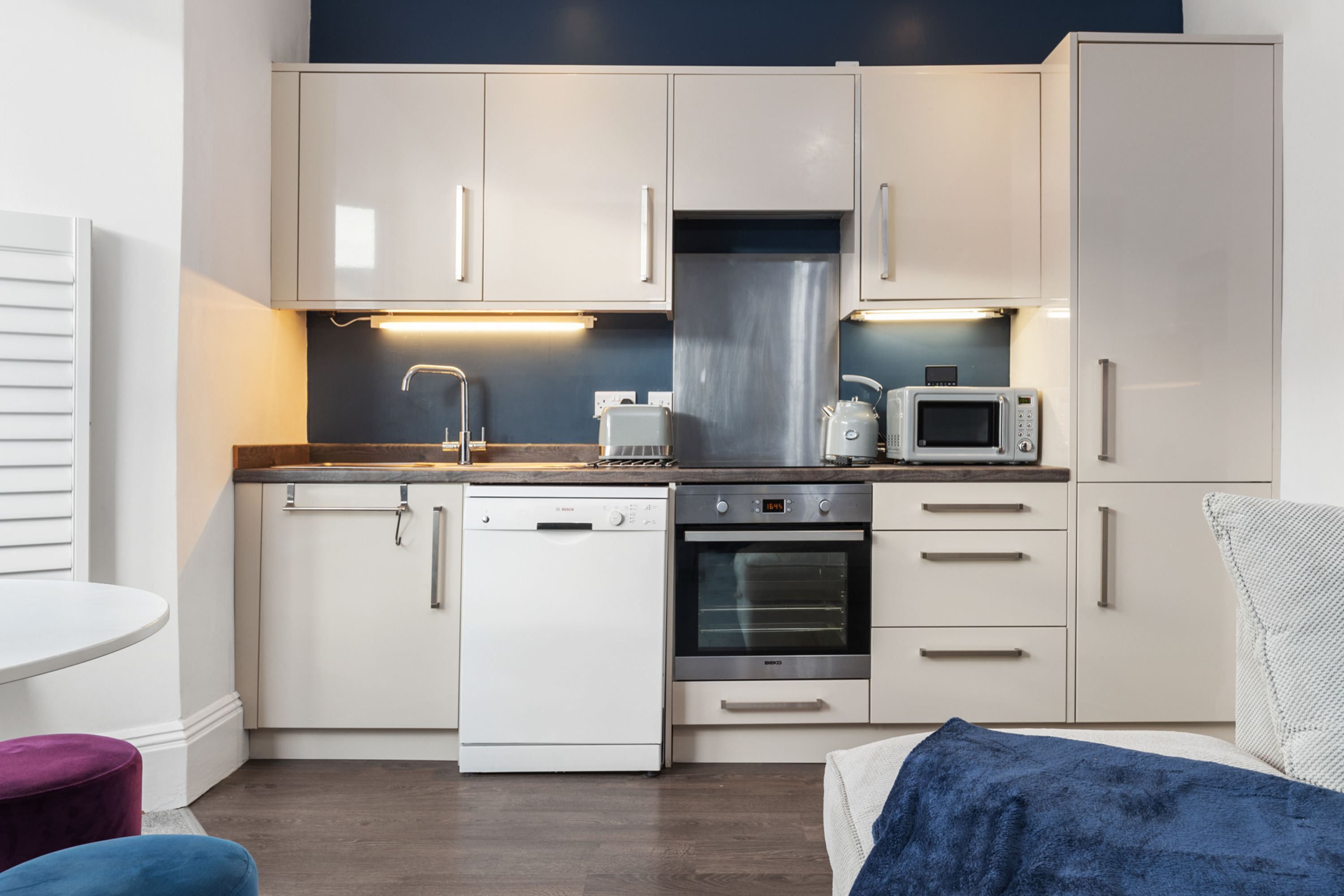Een kleine keuken met witte kastjes, een vaatwasser, oven en magnetron.