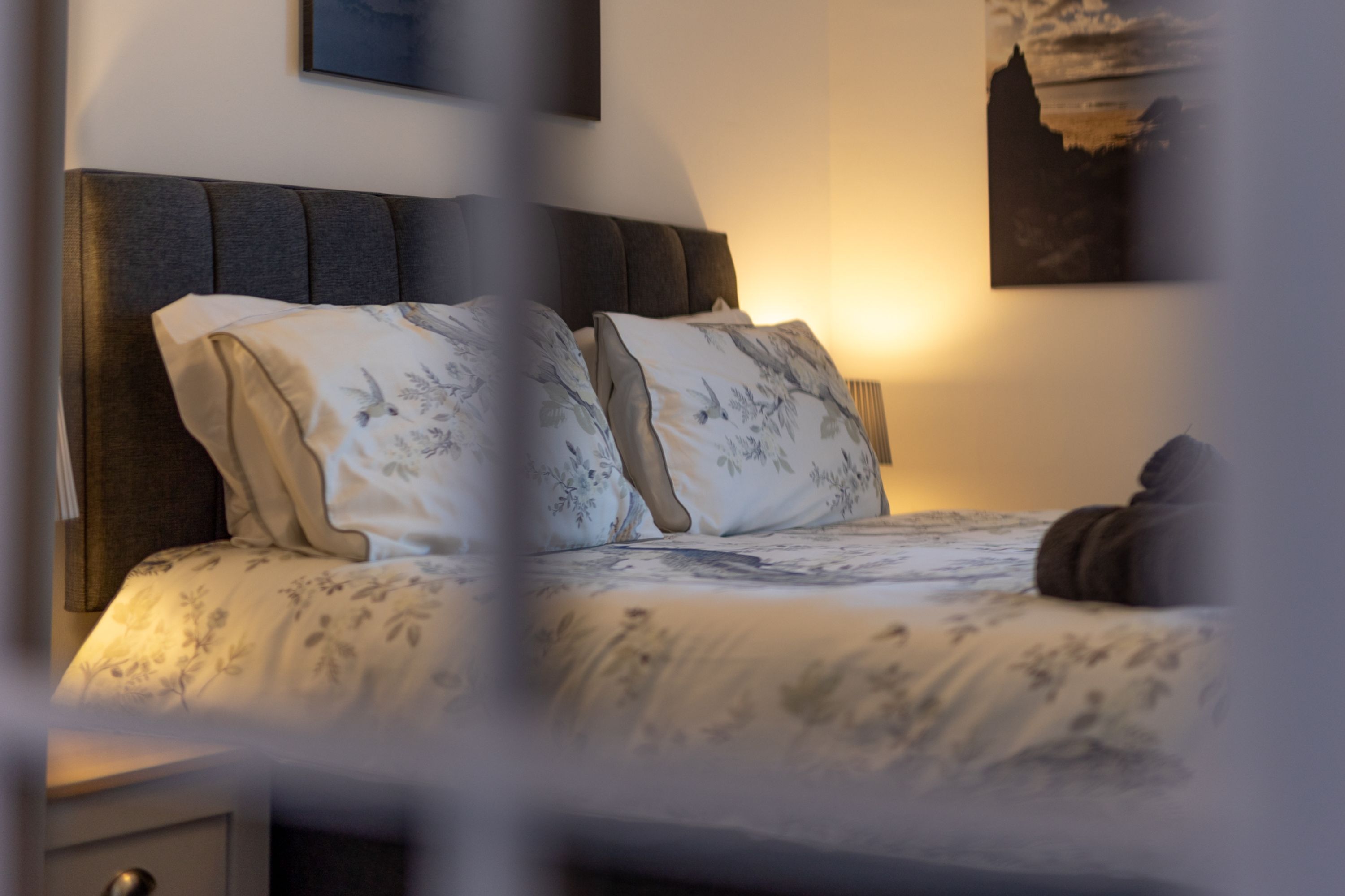 A neatly made bed with floral bedding, a dark headboard, and a wall-mounted artwork.