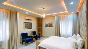 A modern hotel room with a large bed, a desk, and a seating area. - PLUSH HOTEL (Abuja)