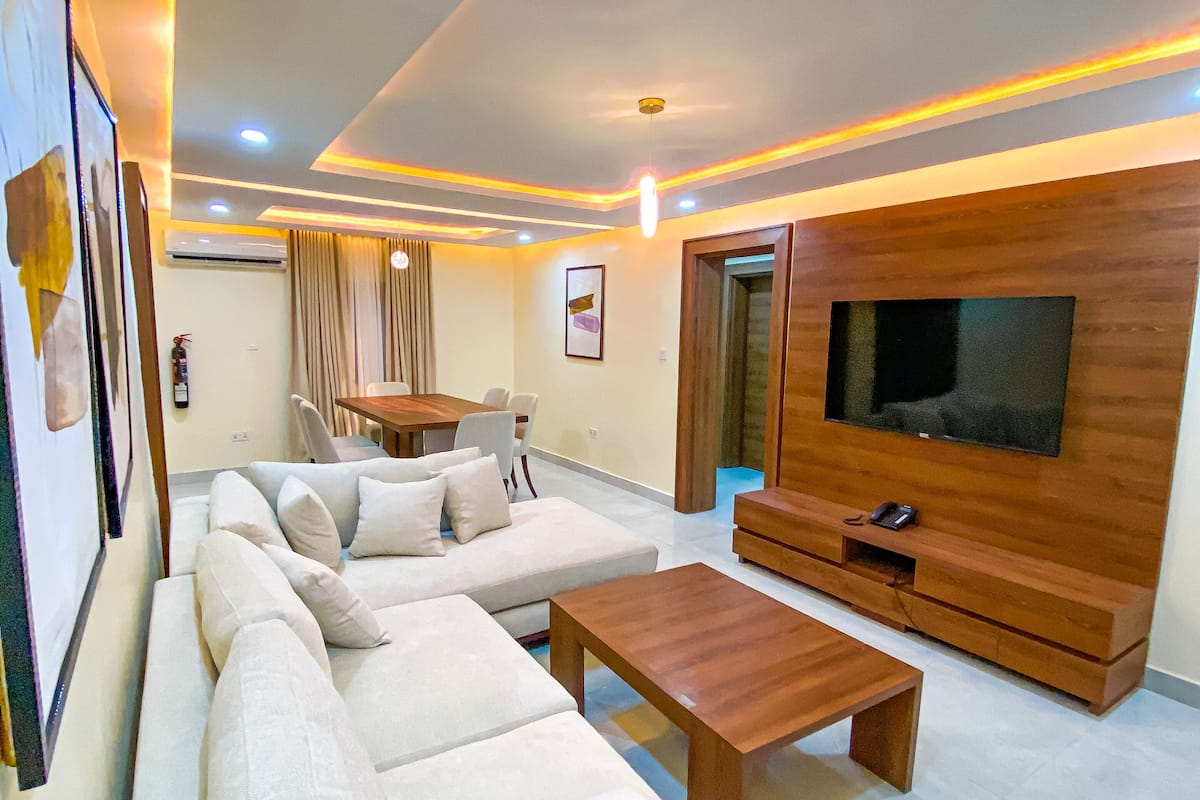 Uma sala de estar moderna com um sofá seccional grande, uma mesa de centro de madeira e uma televisão de tela plana fixada numa parede de madeira.