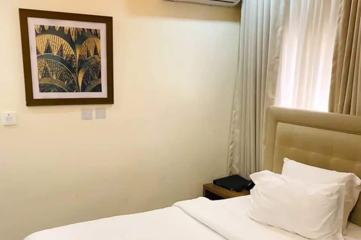 Quarto de hotel com cama, mesa de cabeceira, quadro na parede e janela com cortinas.