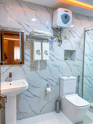 Un baño con salpicadero de mármol, un lavabo, un inodoro, una ducha y un perchero con toallas.
