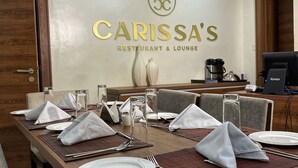 A dining area with a table set for four, a logo above the name 'CARISSA'S RESTAURANT & LOUNGE', and a Kanton device on the table. - PLUSH HOTEL (Abuja)