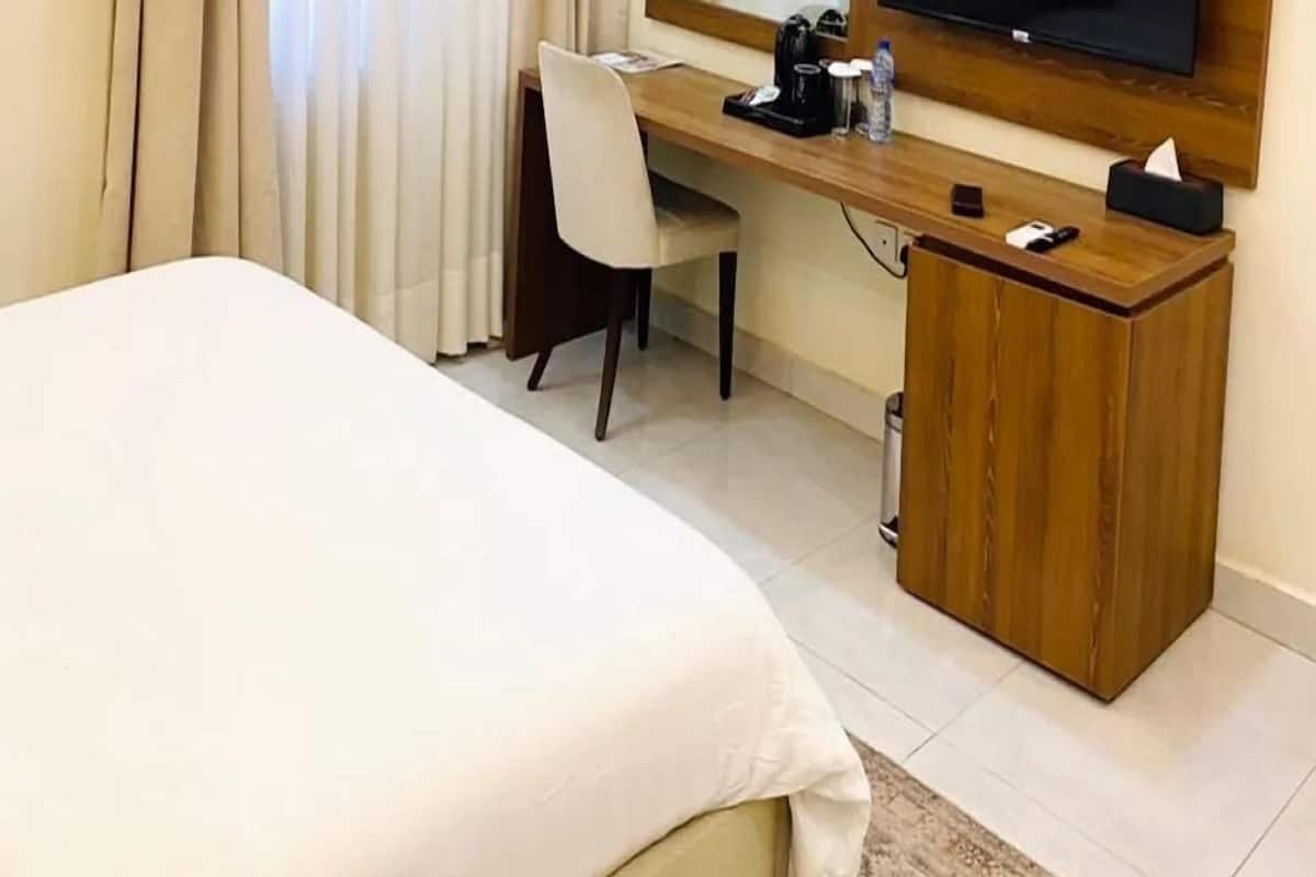 Quarto de hotel com cama, escrivaninha, cadeira, televisão e armário de madeira.