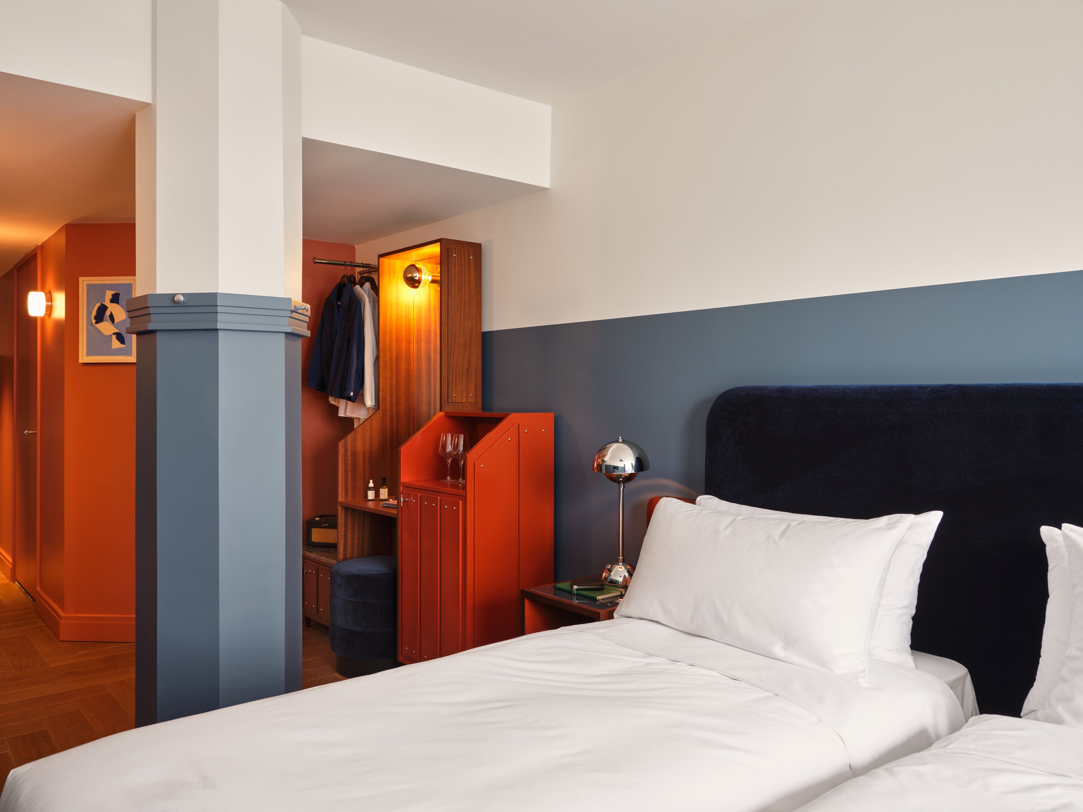 Habitación de hotel con cama, mesita de noche, lámpara, armario y zona de estar con una silla y una mesa.