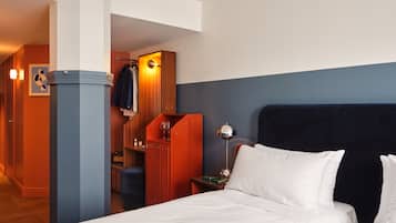 Habitación de hotel con cama, mesita de noche, lámpara, armario y zona de estar con una silla y una mesa.