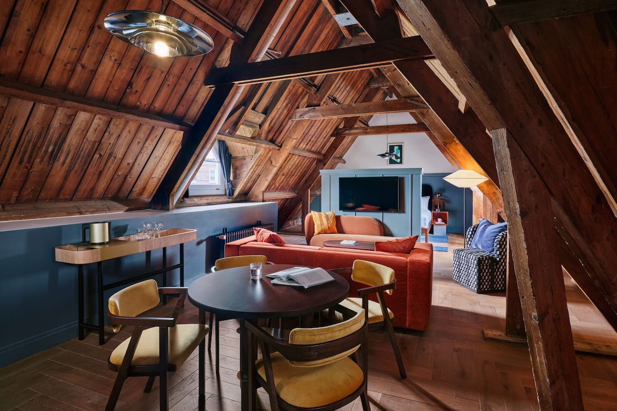 An attic room with a wooden ceiling, a dining table with chairs, a sofa, and a television.
