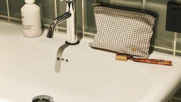 Een wastafel met een chromen kraan, een handzeepfles en een toilettas met een ruitpatroon.