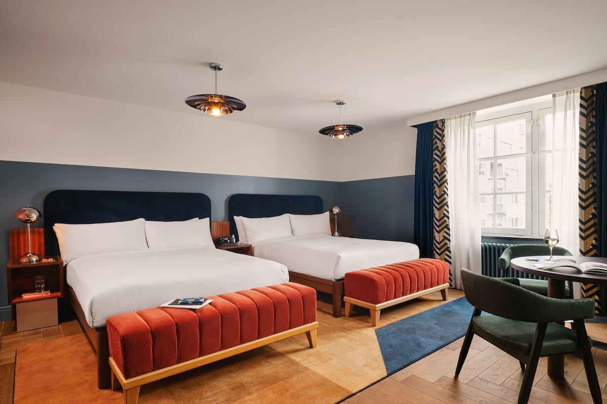 A hotel room with two beds, a dining area, and a view of the city.