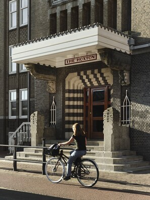 Una mujer montando en bicicleta frente a un edificio con un letrero que dice "THE HOXTON".