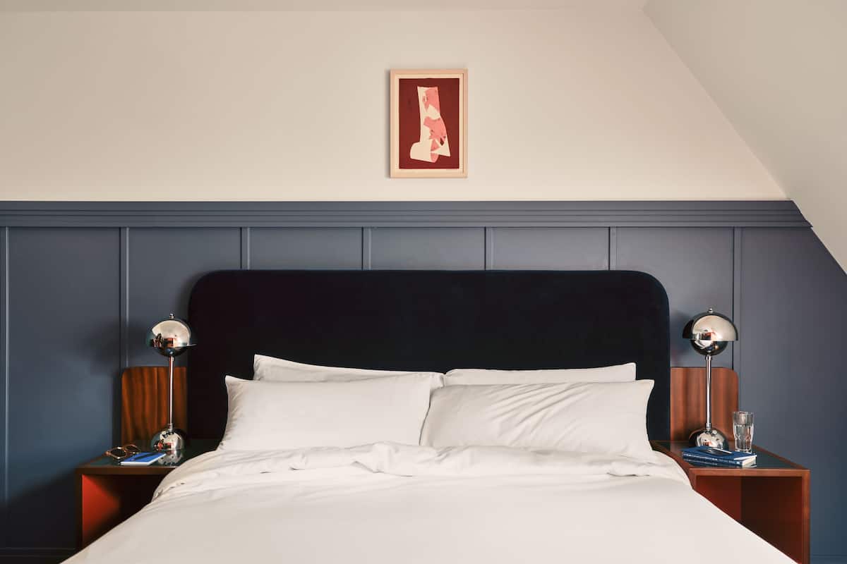 A neatly made bed with white linens, a dark headboard, and two bedside lamps on wooden nightstands.