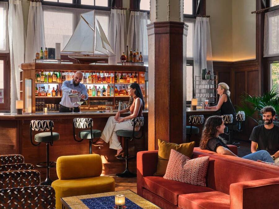A bar area with a wooden bar counter, stools, and a seating area with a red sofa and patterned chairs.