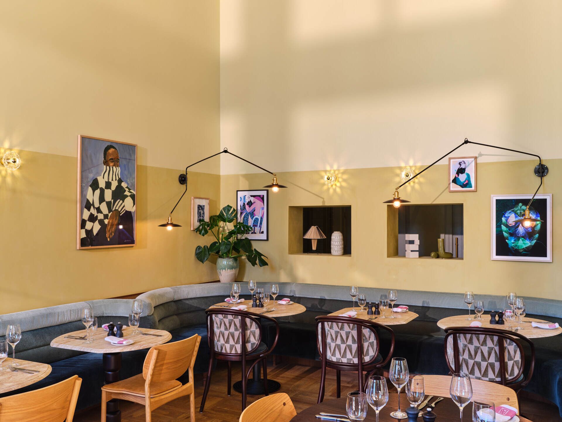 Un restaurante con mesas redondas, asientos tipo banca acolchados y obras de arte colgadas en la pared.