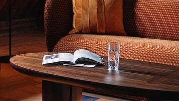 Une pièce chaleureuse avec un plafond en bois, un canapé agrémenté de coussins à motifs, une table basse ronde en bois sur laquelle reposent un livre et un verre d’eau, et un téléviseur fixé au mur.
